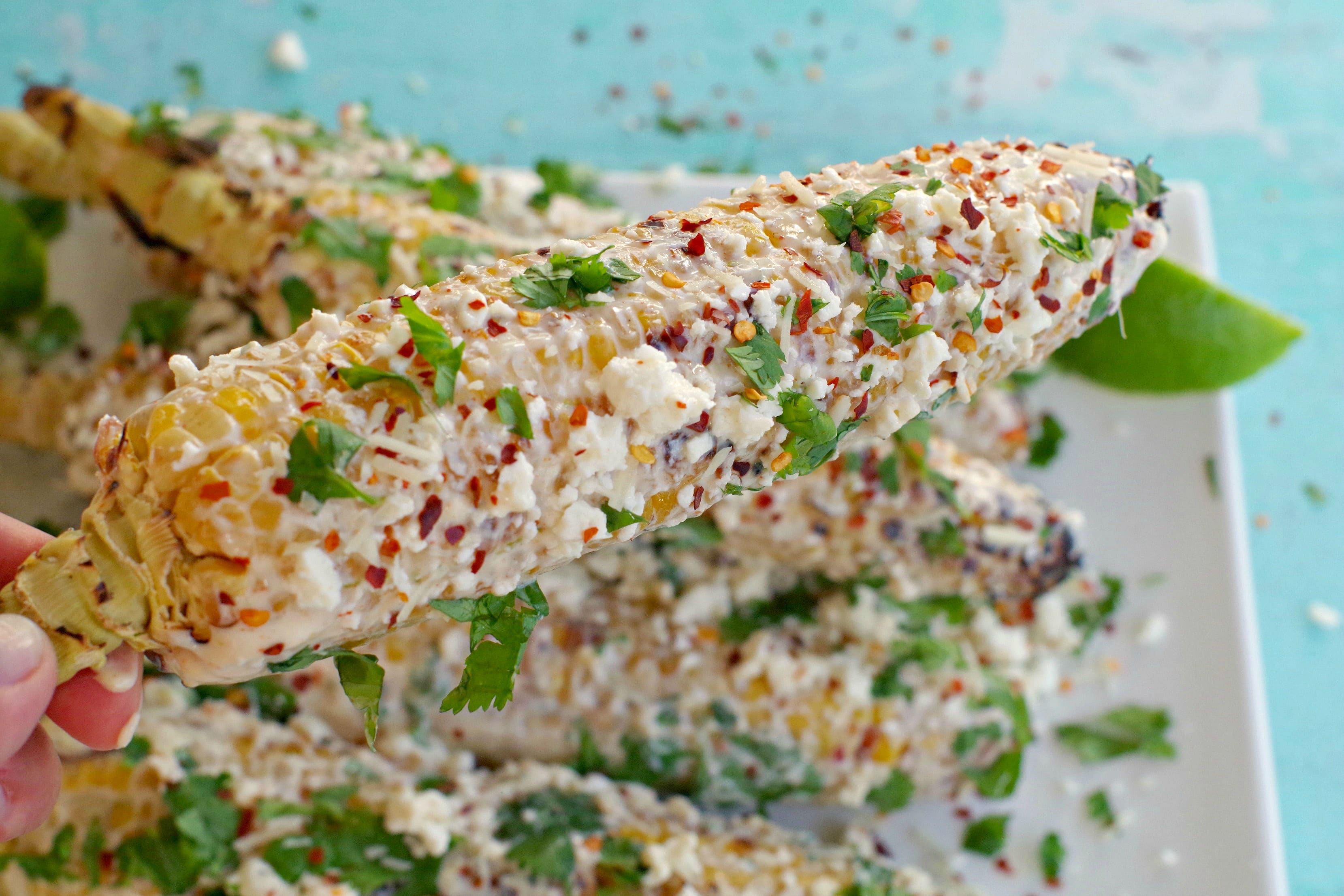 mexican corn on the cob being held up over platter