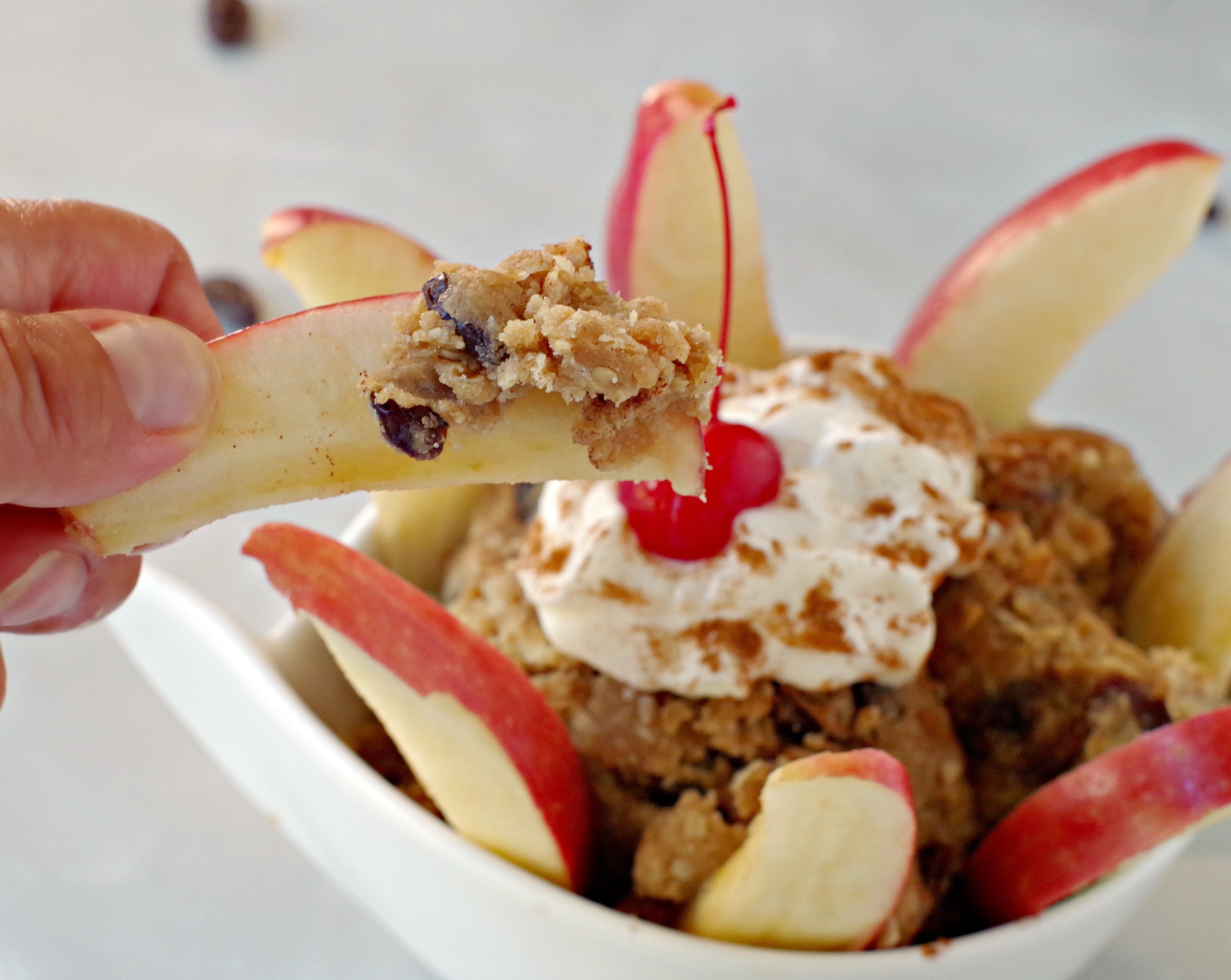 apple piece being dipped into edible oatmeal raisin cookie dip