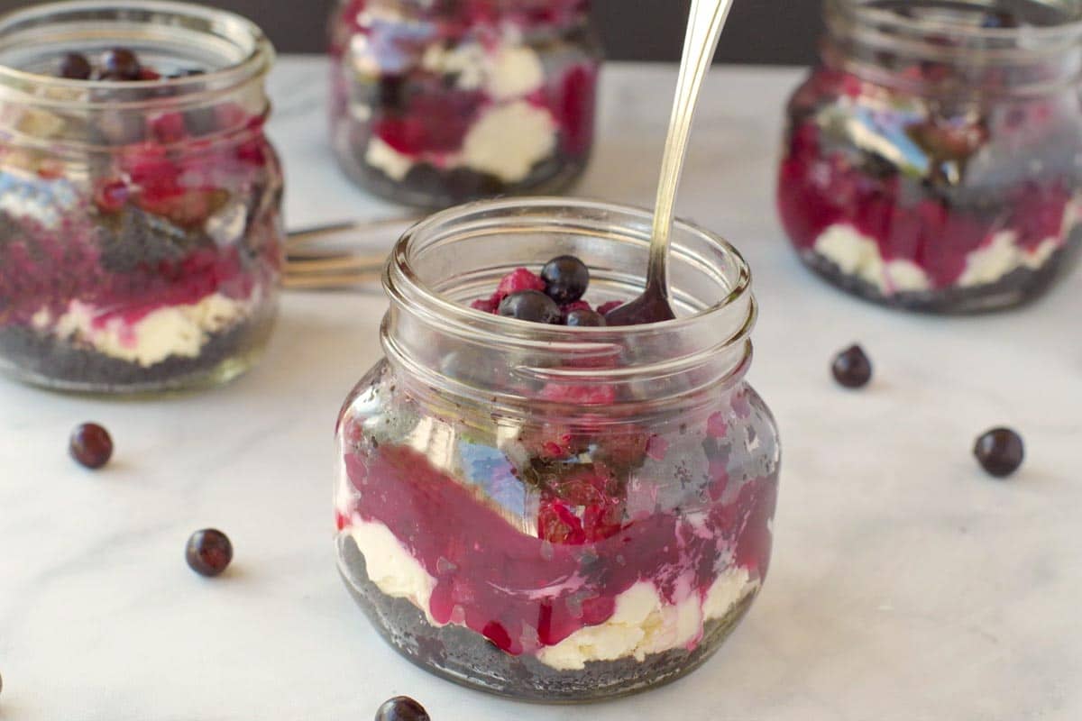 no bake saskatoon berry cheesecake in a jar with a spoon and more jars in the background