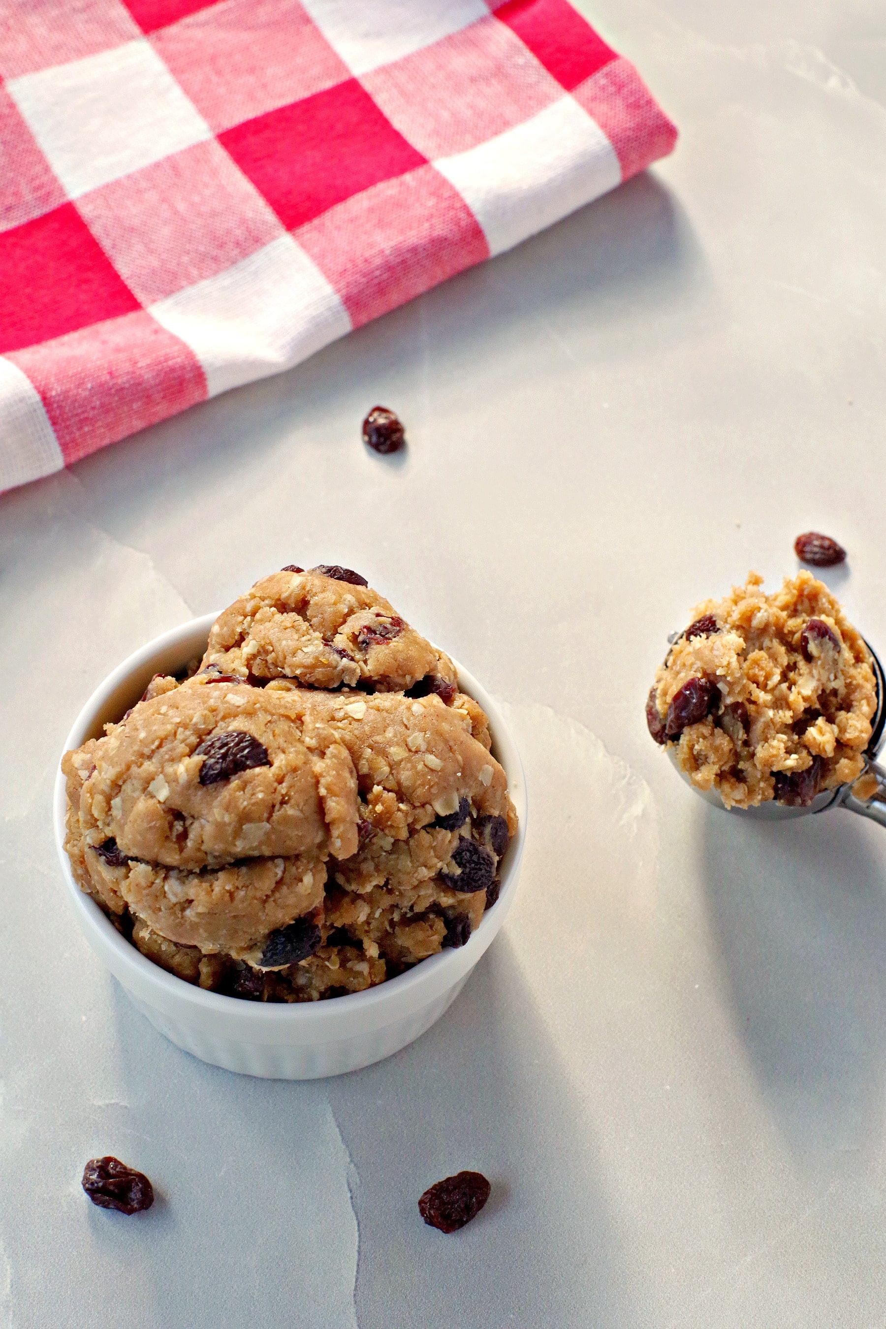 edible cookie dough in white bowl with cookie scoop beside it