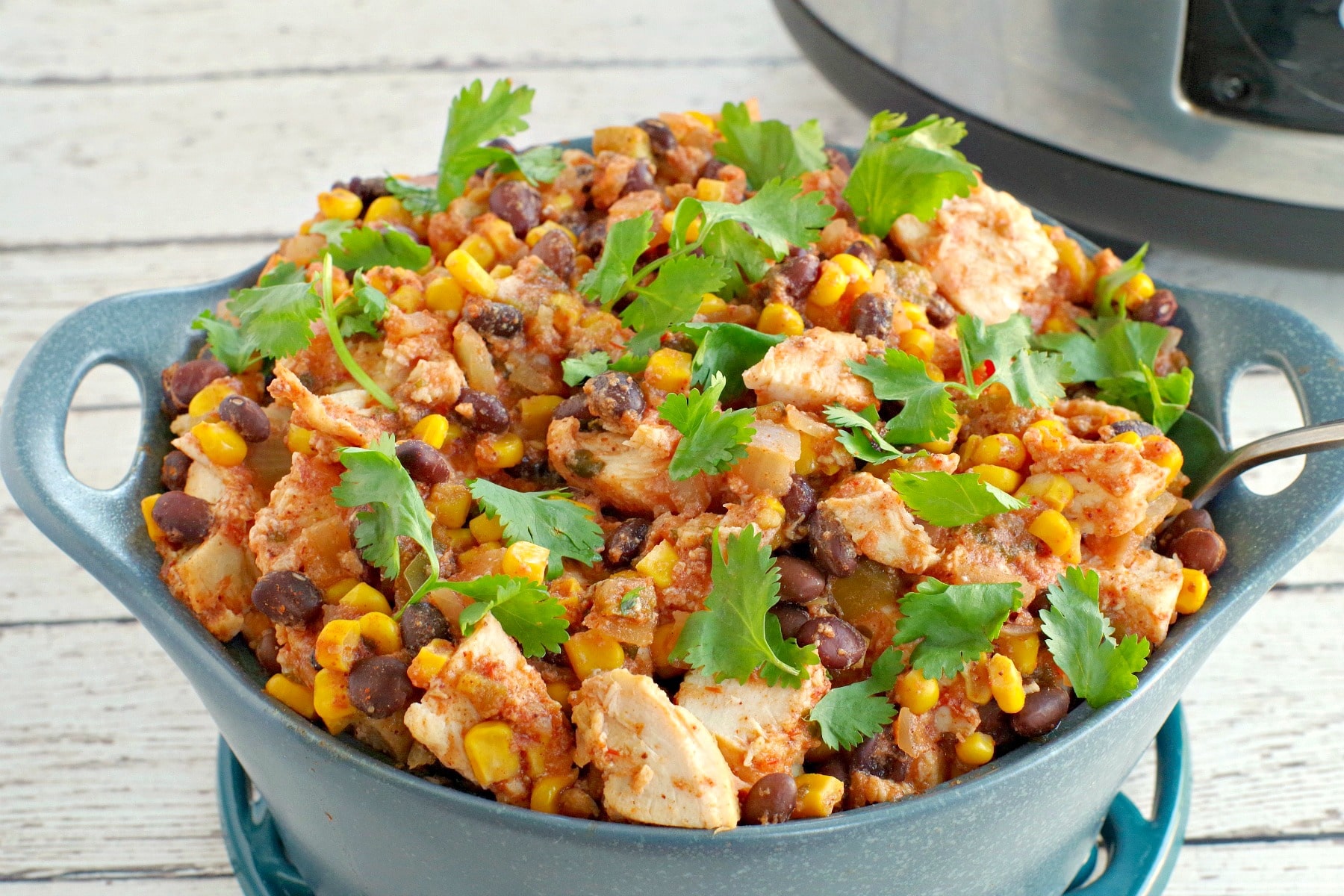 slow cooker mexican chicken in a blue dish with slow cooker in background