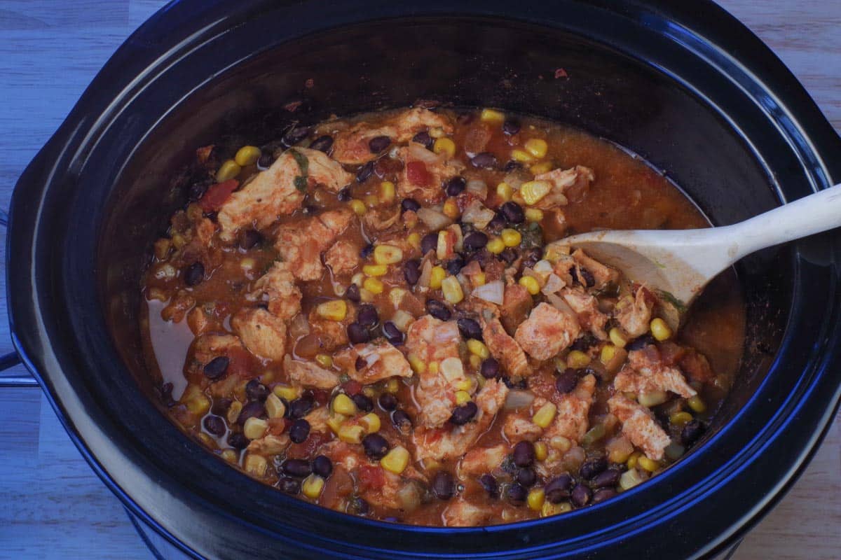 cooked Mexican chicken in crockpot with wooden spoon.