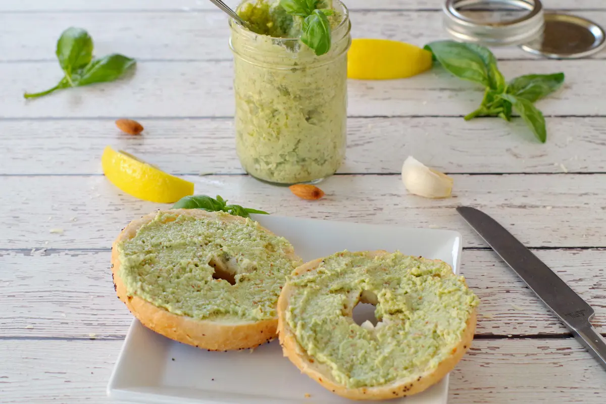 basil almond pesto on bagel with a jar of pesto in the background
