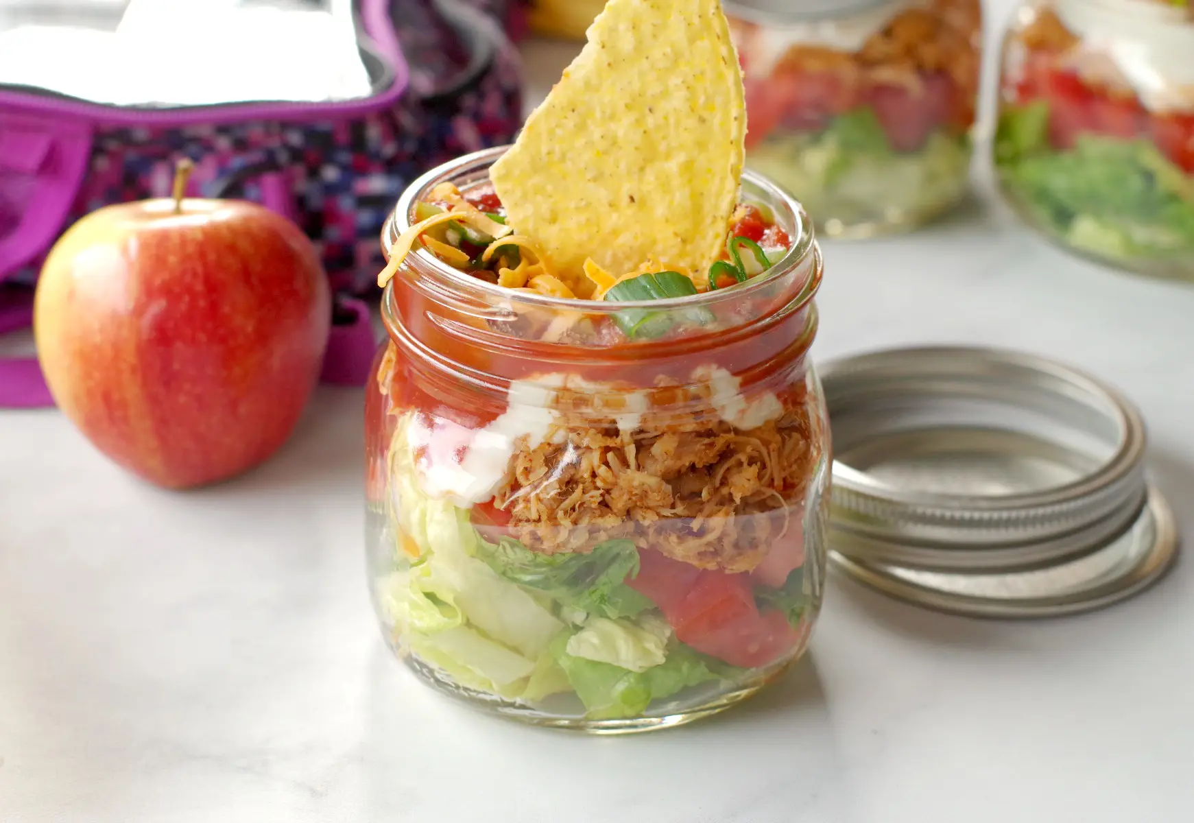 chicken taco salad in a mason jar with more jars, an apple and lunch bag in background