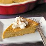 crustless pumpkin pie on a white plate with fork and whole pie in background