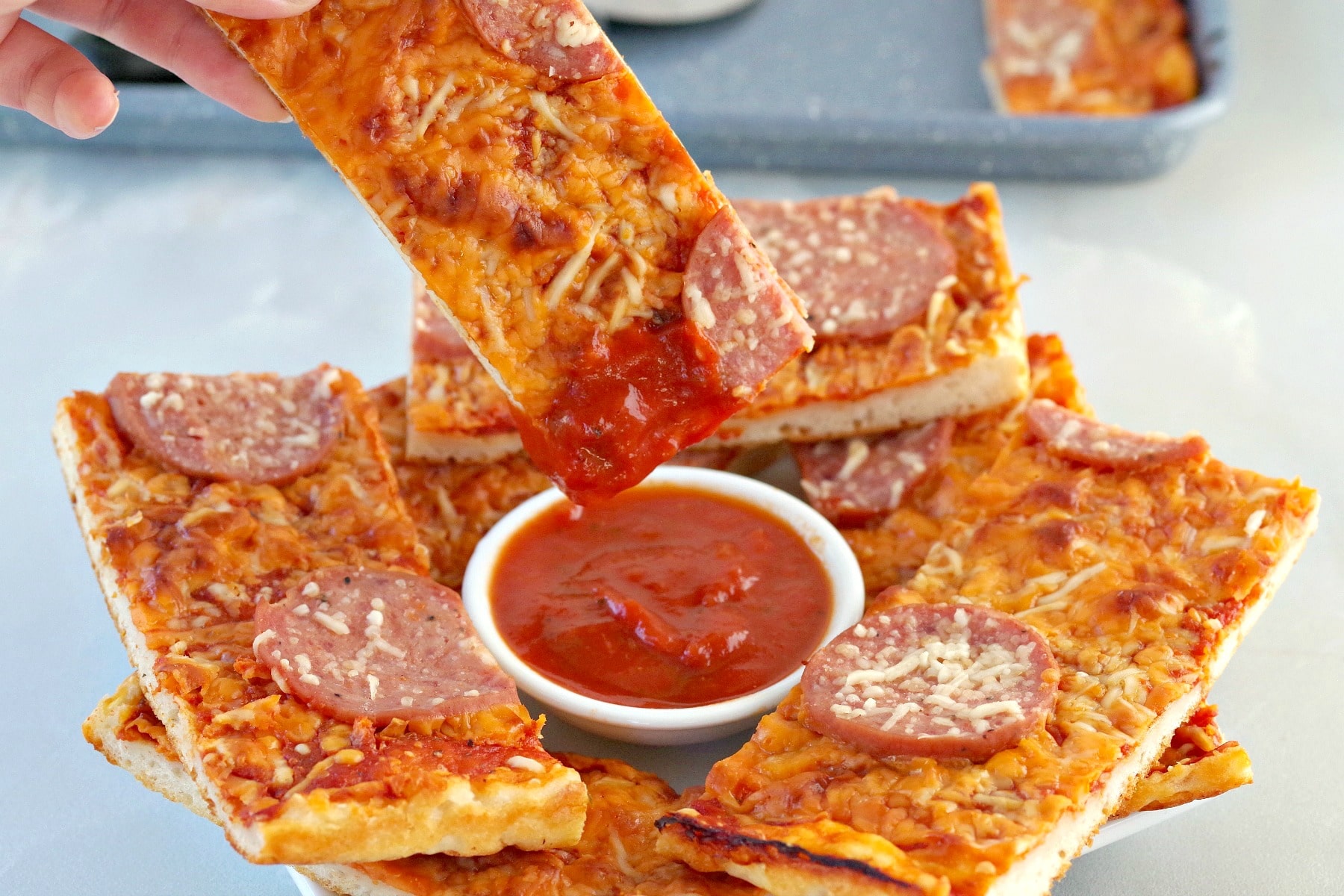 pizza dipper being dipped into piece sauce with other pizza dippers surrounding it on plate