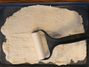 dough being rolled out onto cookie sheet