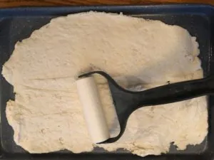 dough being rolled out onto cookie sheet
