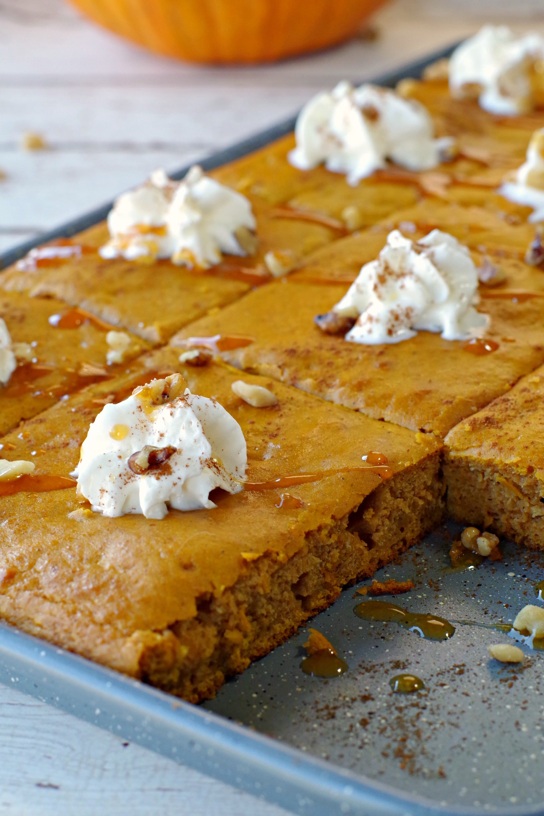 pumpkin spice pancakes on a sheet pan with one pancake missing and pumpkin in background