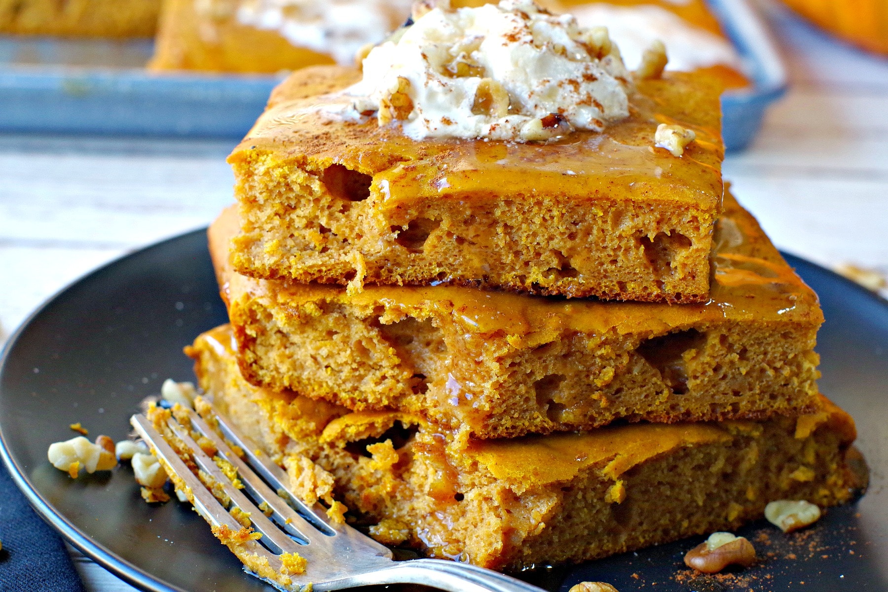 stack of 3 pumpkin pie pancakes on black plate with bite eaten out of stack and fork on the side