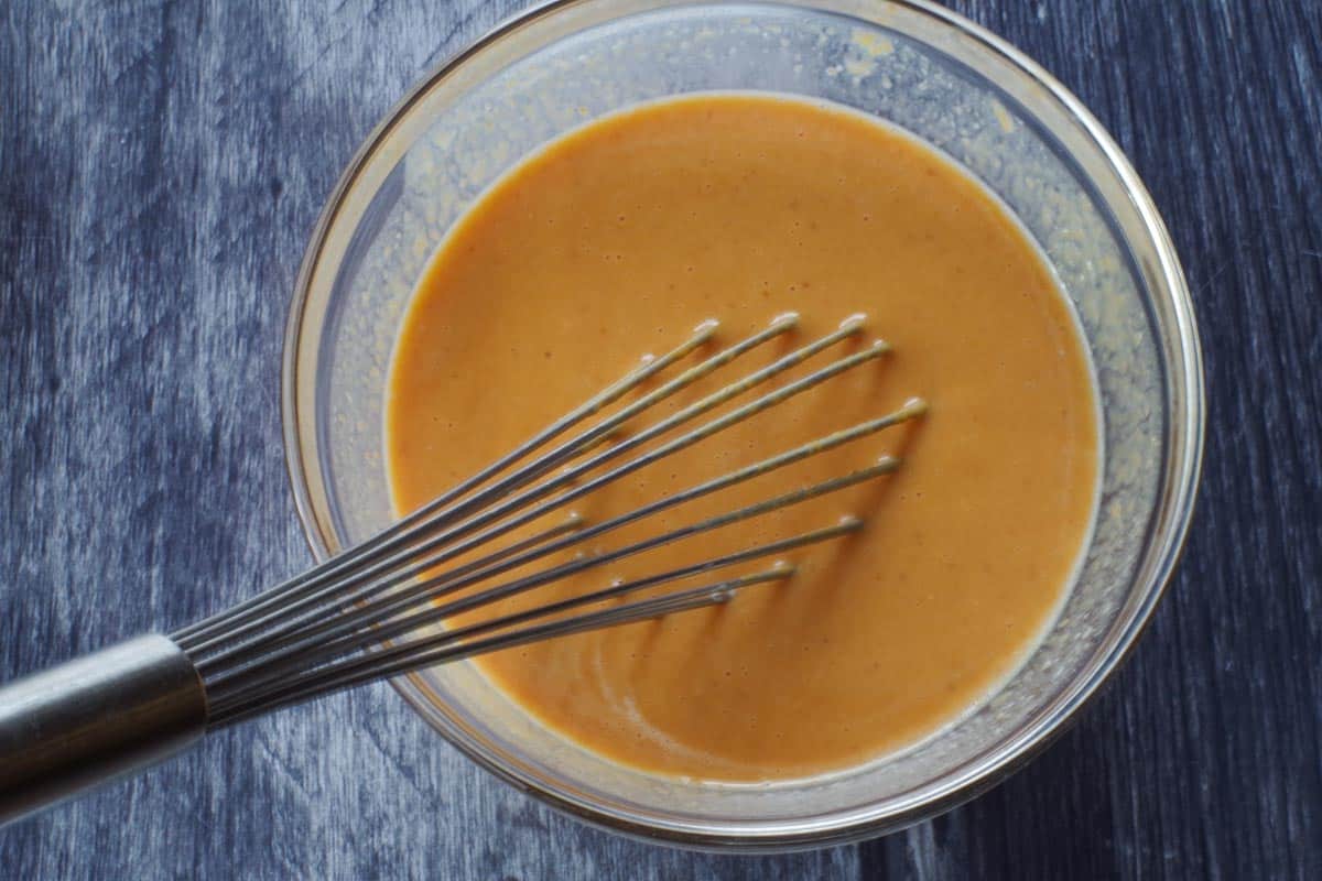 cooled scalded milk added to pumpkin mixture in a glass bowl with a whisk