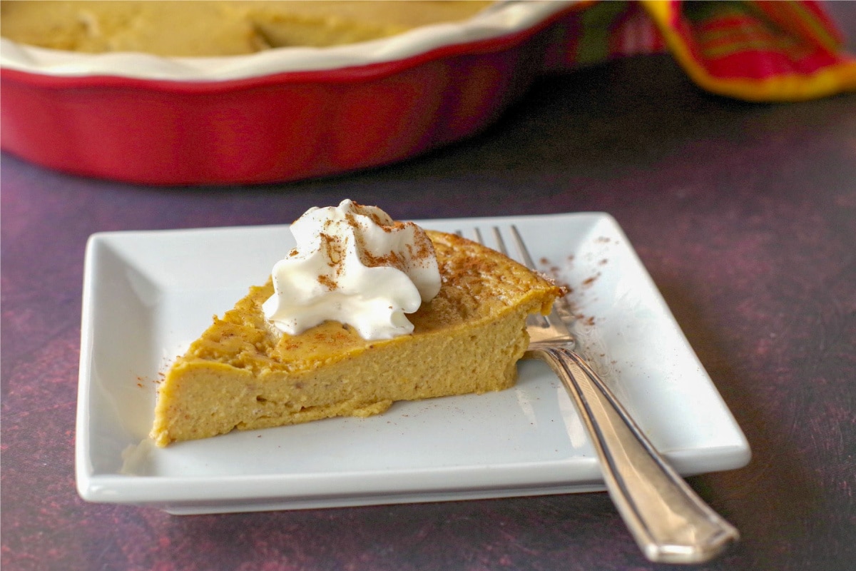 crustless pumpkin pie on a white plate with fork and whole pie in background