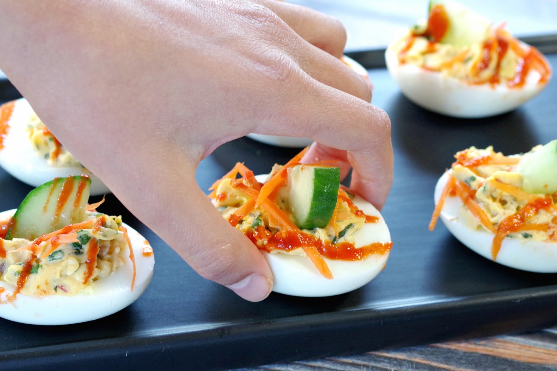 banh mi devilled egg being grabbed off black tray with child's hand