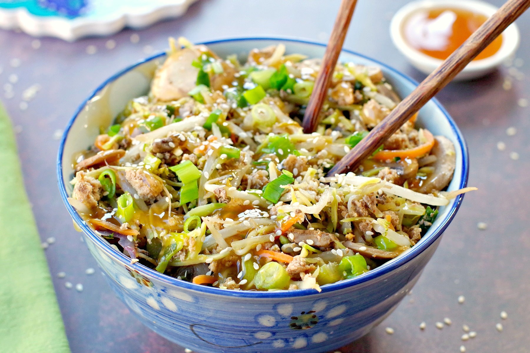 egg roll in a blue flowered bowl with chopsticks and a small white dish of plum sauce in the background