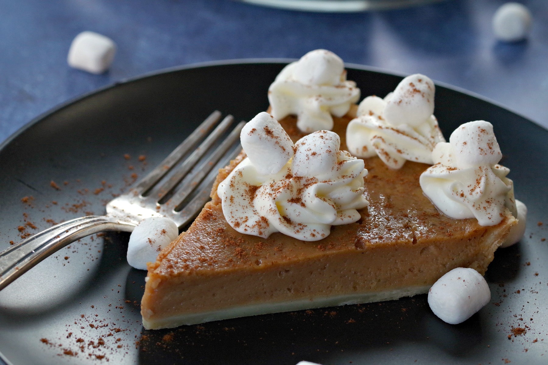 sweet potato pie on black plate on blue background with marshmallows around