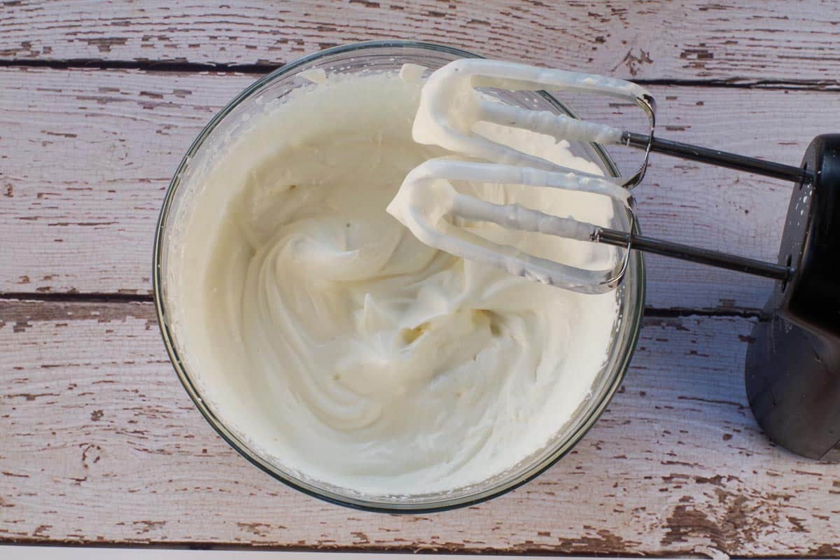 Whipping cream whipped to soft peaks in a medium glass bowls, with beaters above the bowl.