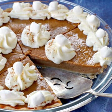 Sweet potato pie with marshmallow whipped cream in glass pie plate with piece missing and pie lifter in missing spot.