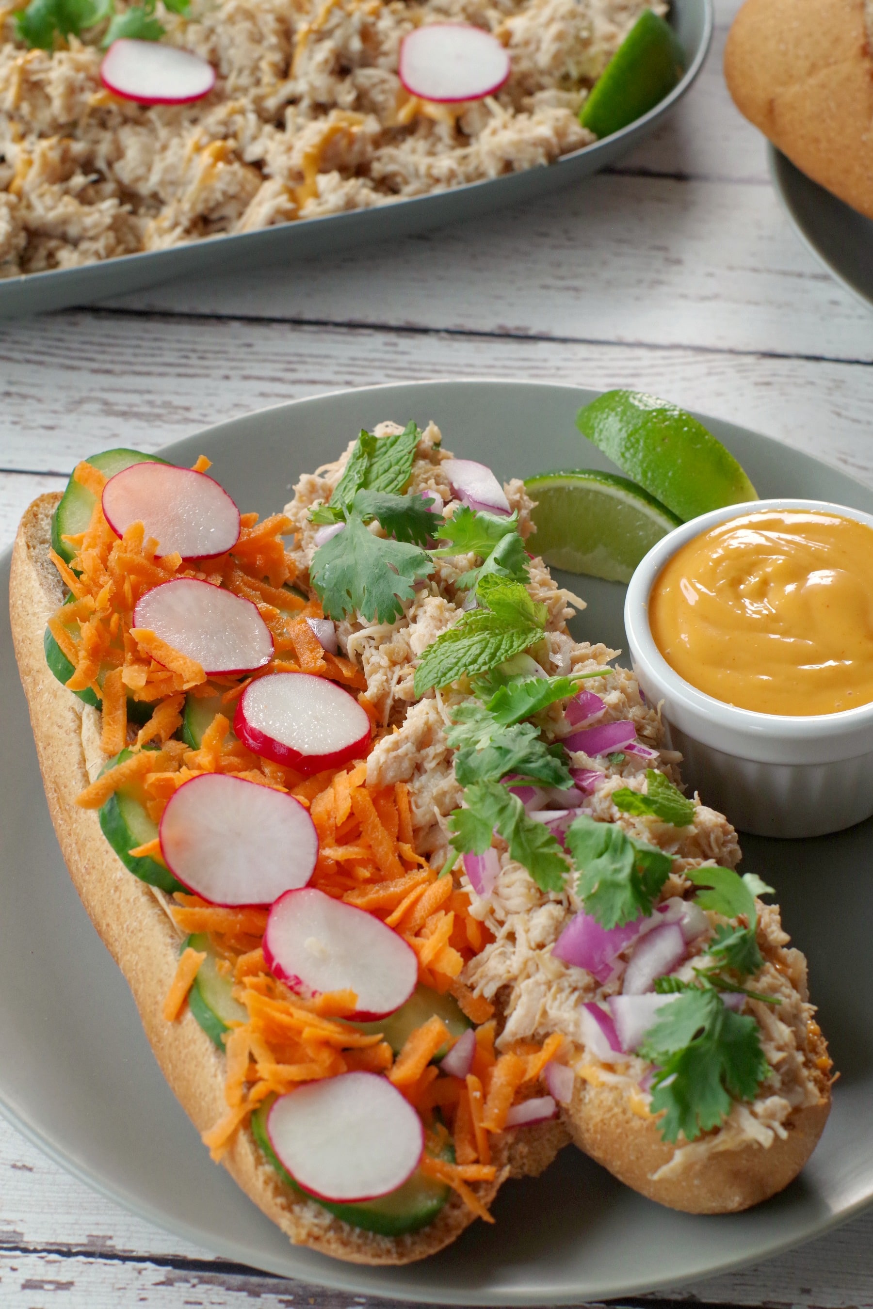 open chicken banh mi vietnamese sub on a greenish grey plate with lime garnish and small white dish of sriracha mayonnaise