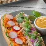 pin with text on top and bottom and photo ofopen chicken banh mi vietnamese sub on a greenish grey plate with lime garnish and small white dish of sriracha mayonnaise