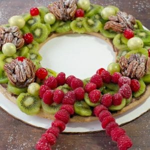 gingerbread fruit wreath on a white cardboard cake platter on a brown faux wooden surface