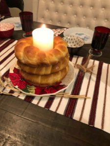 3 Kolach stacked, with a candle in the middle on a table with dinner plates and a striped red and white table runner