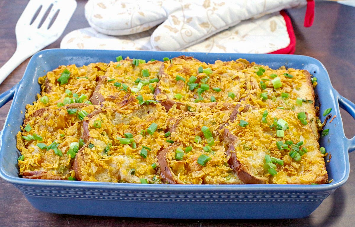 Christmas breakfast casserole in blue casserole dish with white and gold Christmas oven mitts in the background