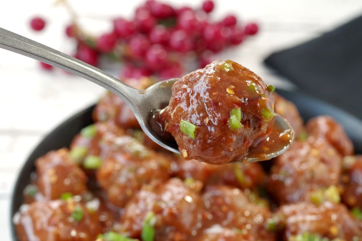 slow turkey turkey meatballs in a black bowl with a meatball being held up on a spoon
