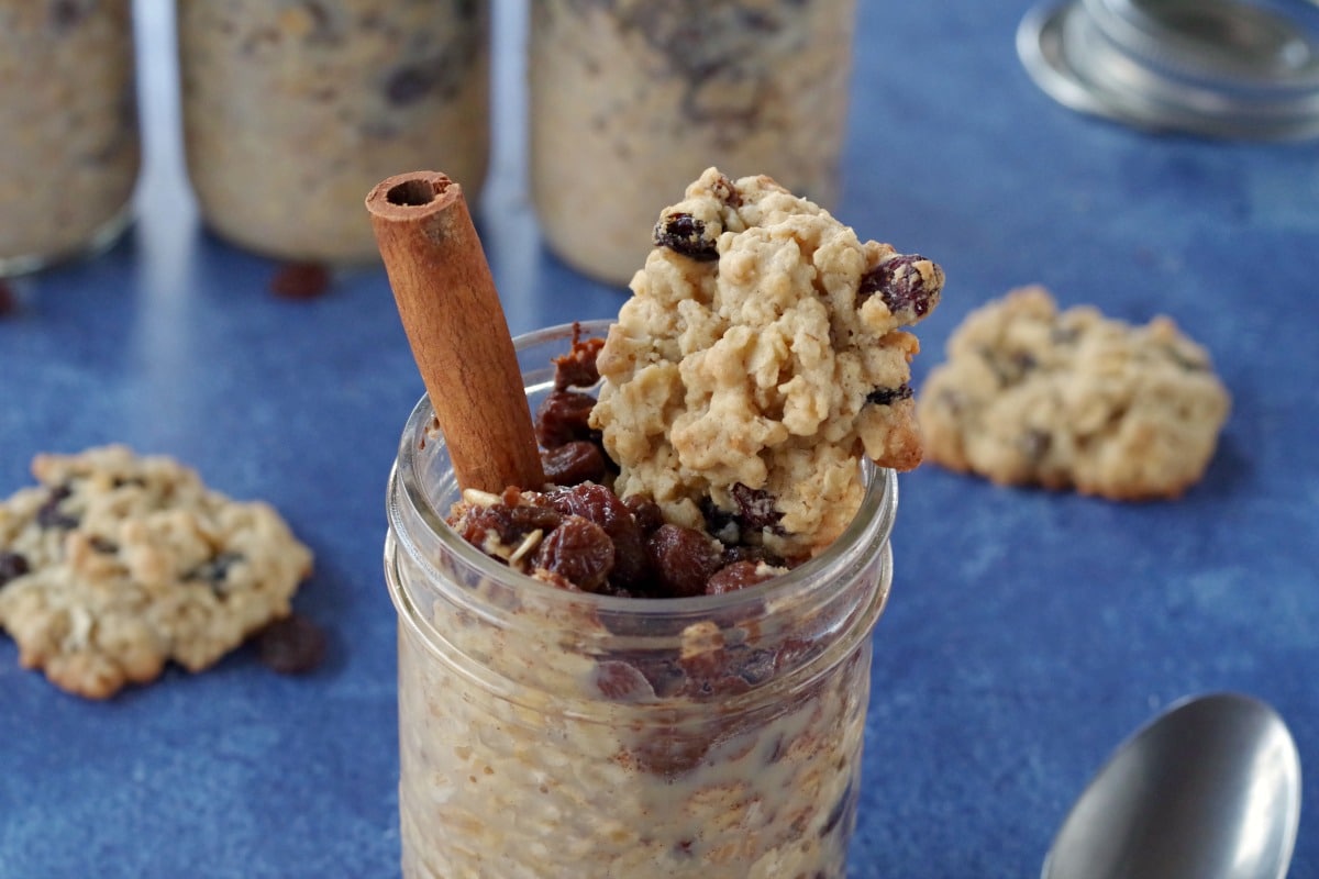 raisin cookie oatmeal in a jar with cookie on top on blue background with raisin oatmeal cookies around and jars of oatmeal in background