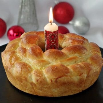 Kolach Ukrainian Christmas Bread on black platter with Ukrainian candle in the middle and Christmas decorations in the background