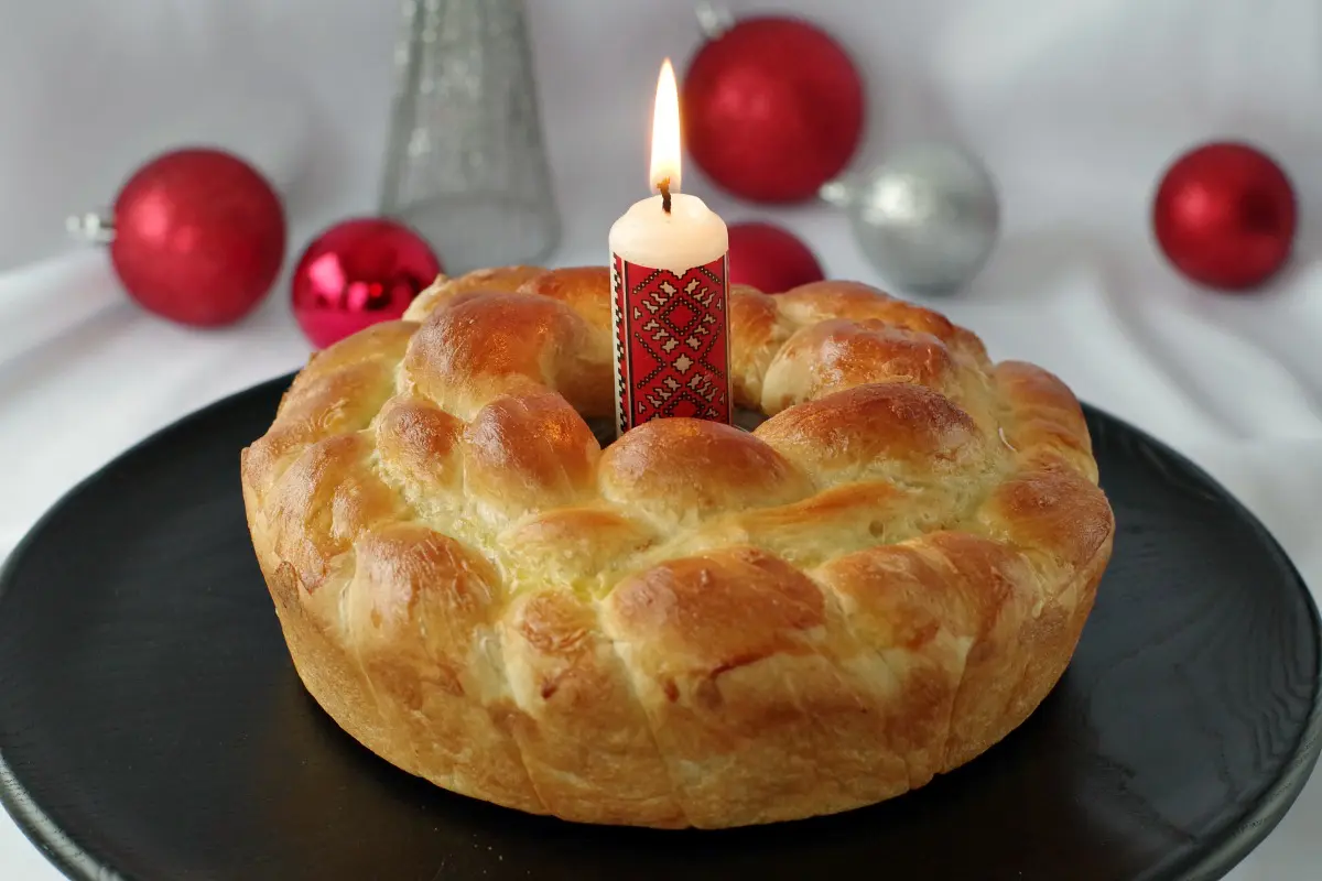 Kolach Ukrainian Christmas Bread on black platter with Ukrainian candle in the middle and Christmas decorations in the background