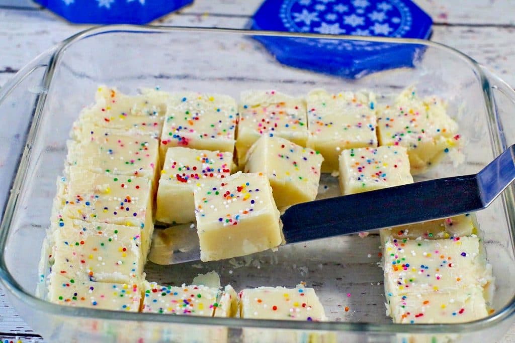squares of sugar cookie fudge in a glass container with a spatula lifting on out