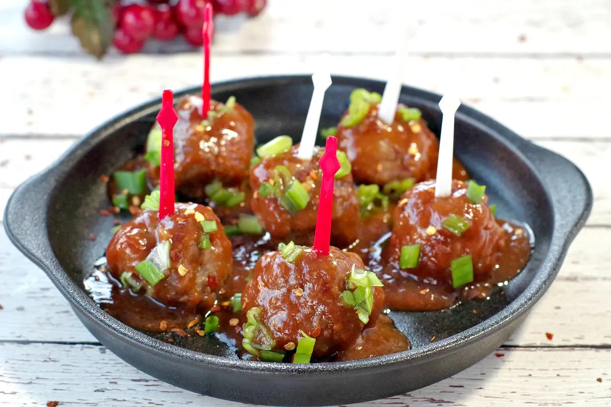 6 slow cooker turkey meatballs with red and white skewers on a black, round serving platter