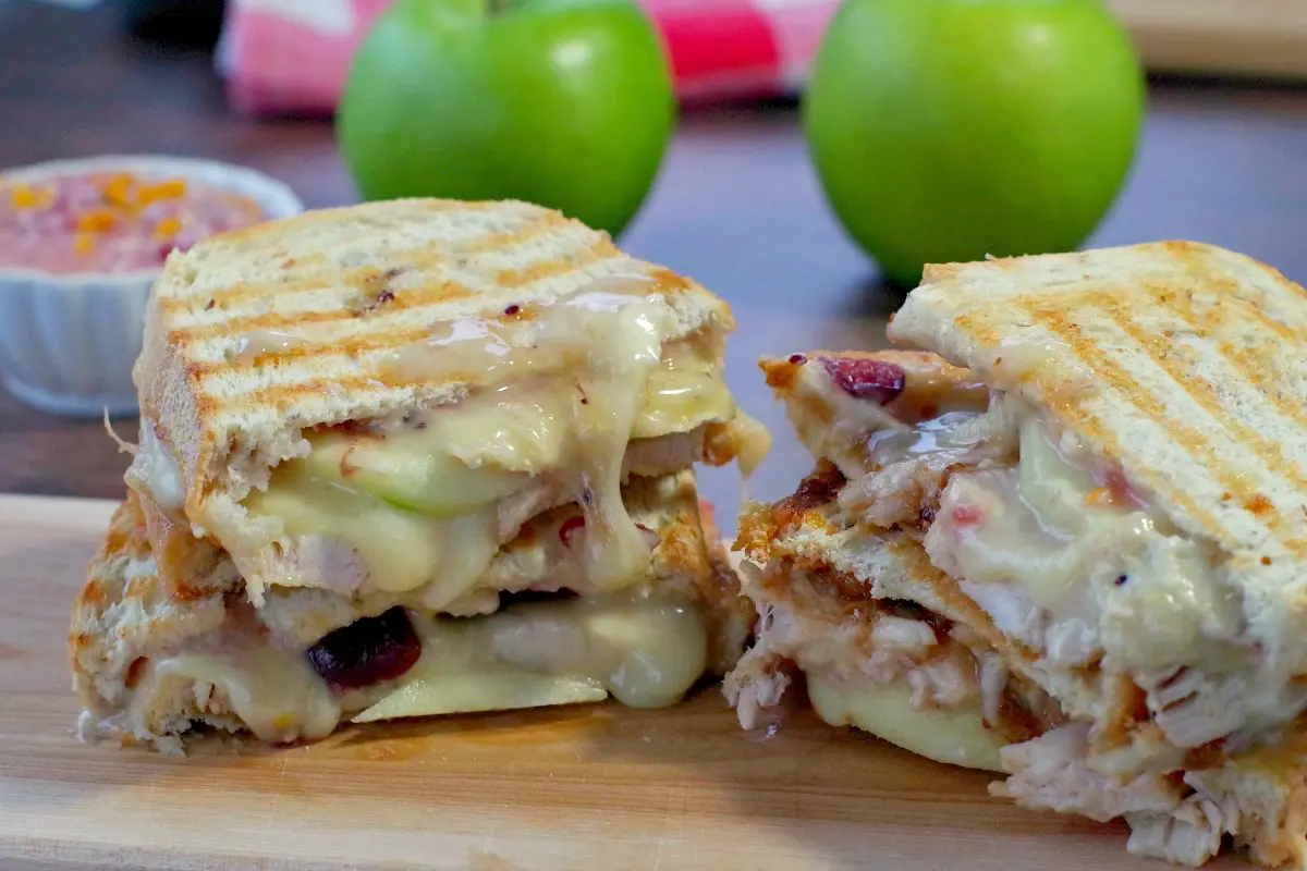 turkey and cranberry panini on cutting board with green apples and cranberry aioli in background