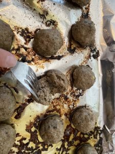 cooked meatballs on baking sheet, with one being cut into
