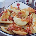 cottage cheese perogies with bacon and onion on a Ukrainian plate, on brown faux wooden surface
