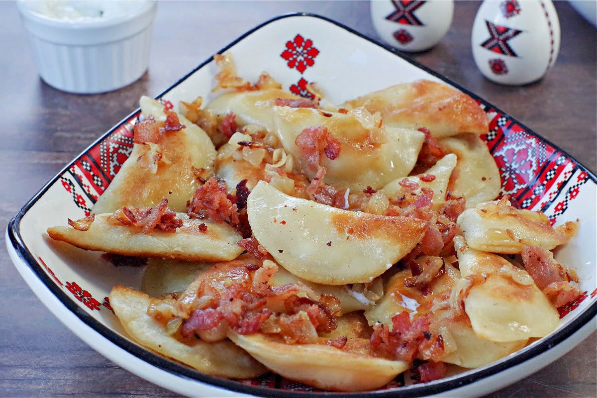 cottage cheese perogies with bacon and onion on a Ukrainian plate, on brown faux wooden surface