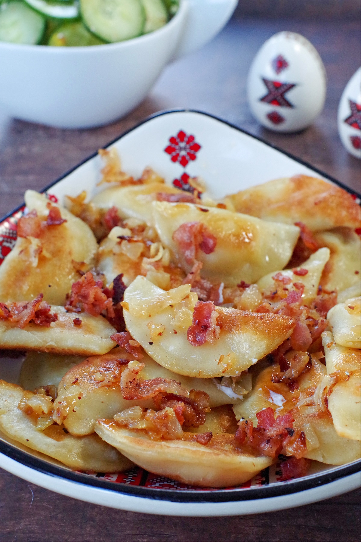Ukrainian perogies covered in bacon and onion in a ukrainian print dish