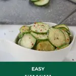 Pinterest pin with white text on green background on top and bottom and photo of cucumber kimchi in white bowl in the middle and a grey cutting board in the background with cucumbers on it