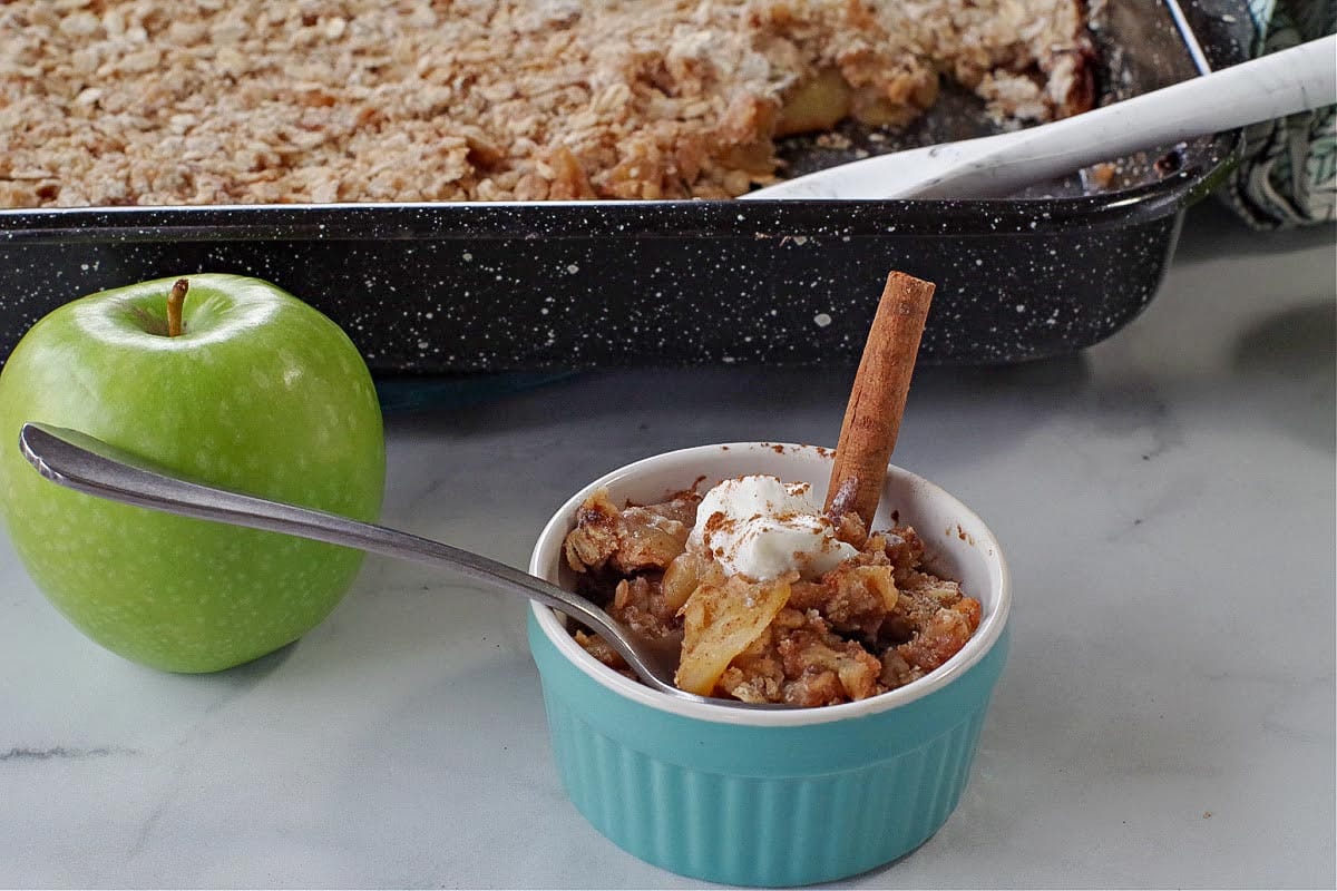 ww apple crisp in a small blue dish with green apple and pan of more apple crisp in the background