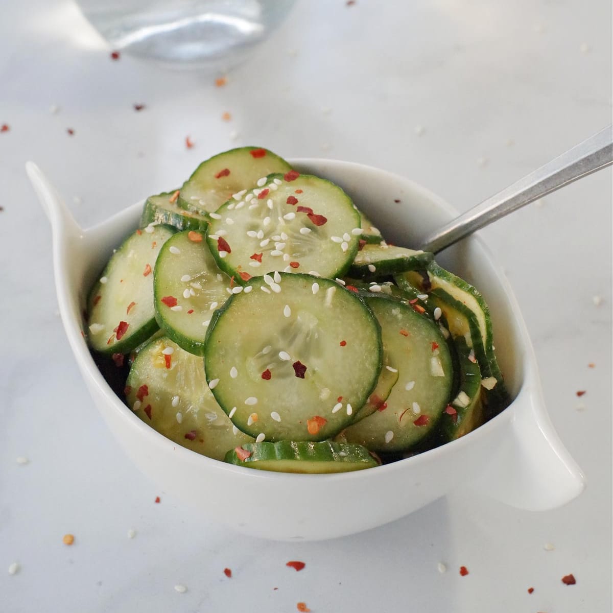 Korean pickles cucumbers in white bowl on grey marble counter surface with glass vinegar container in background