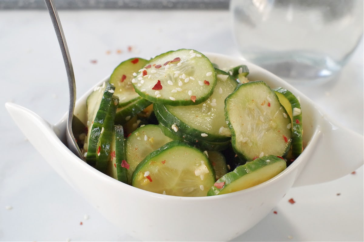 kimchi pickle in white bowl on grey marble counter surface with glass vinegar container in background