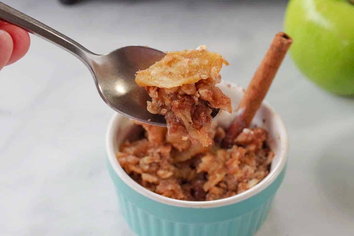 ww apple crisp in small blue dish with spoonful being held up over dish