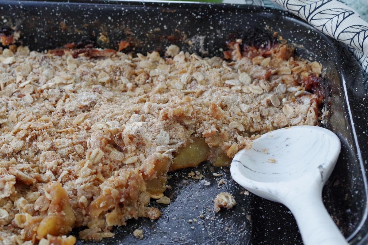 pan of ww apple crisp with ⅓ missing and white marbled silicone spoon in pan