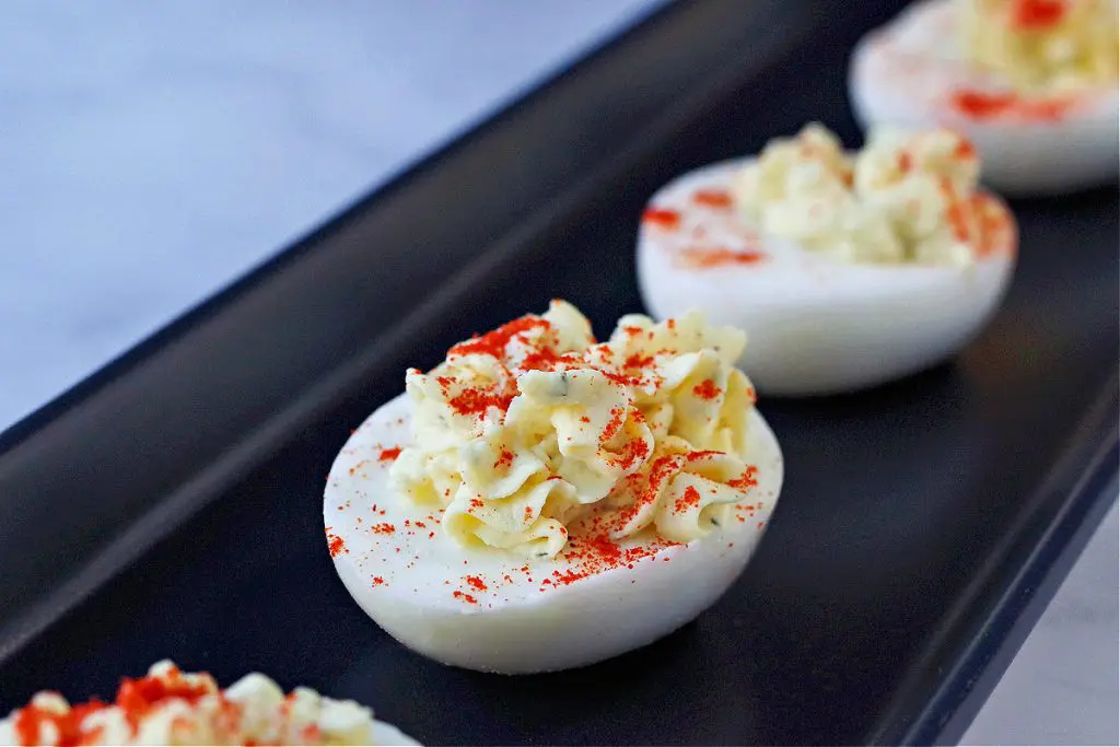 deviled egg with paprika sprinkled on top on black serving tray