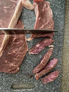 steak being cut into strips on a grey cutting board