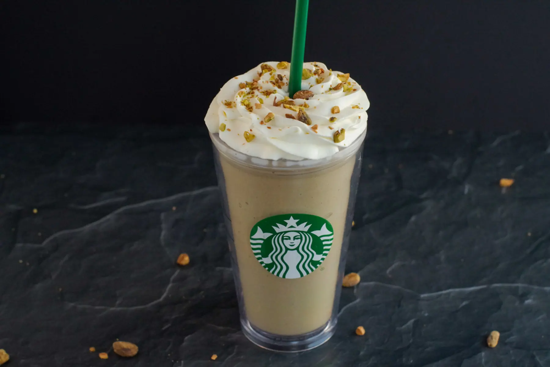 Pistachio Frappuccino in Starbucks cup on black surface with pistachios around