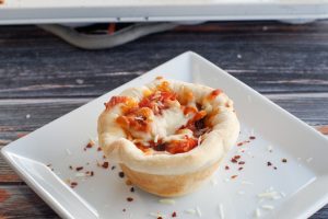 Pizza cupcake on a white plate with crushed red pepper and parmesan cheese sprinkles on plate