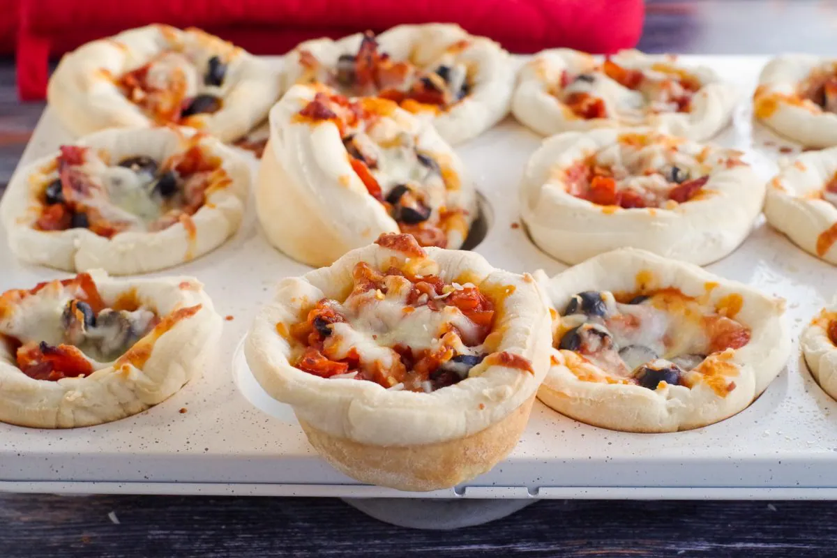 one pizza cupcake sitting on muffin tin with other pizza cupcakes in the muffin tin