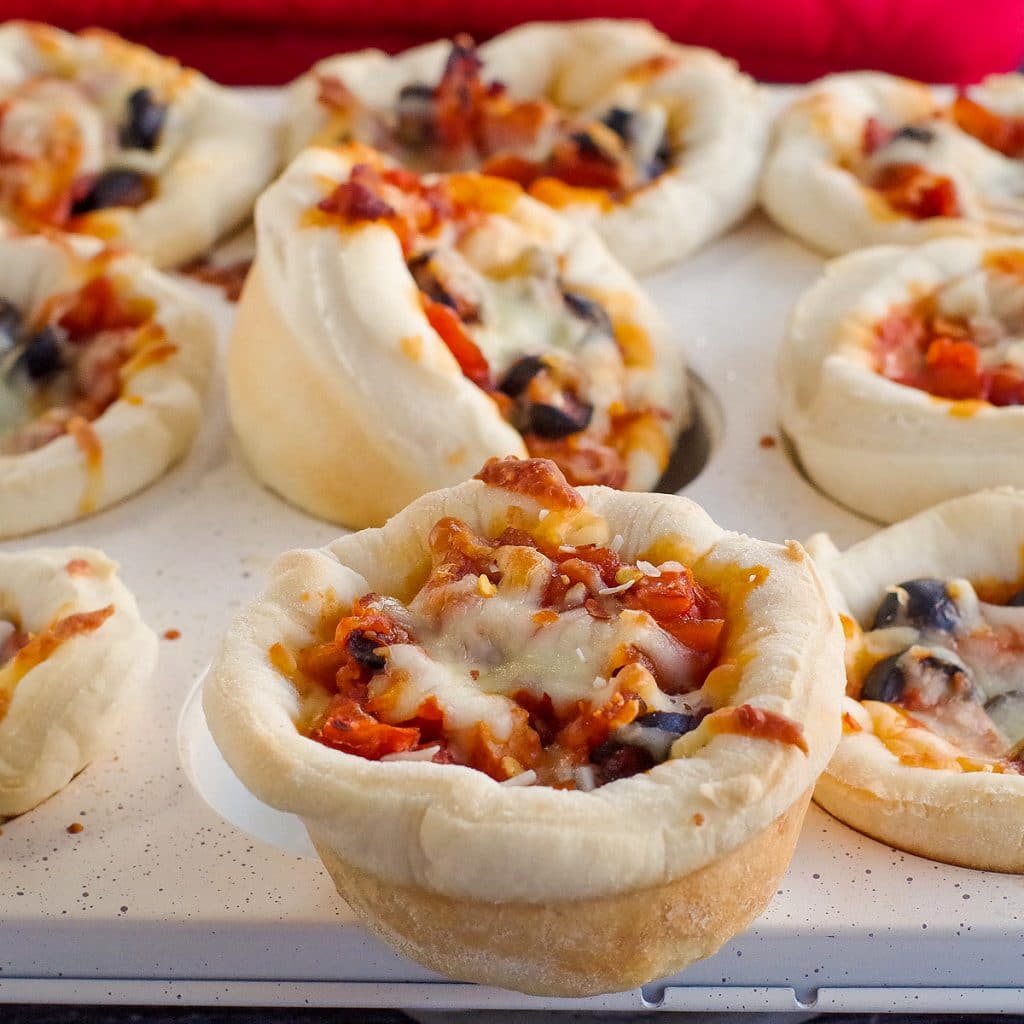 a muffin tin full of pizza cupcake with one pizza cupcake sitting on top in the front