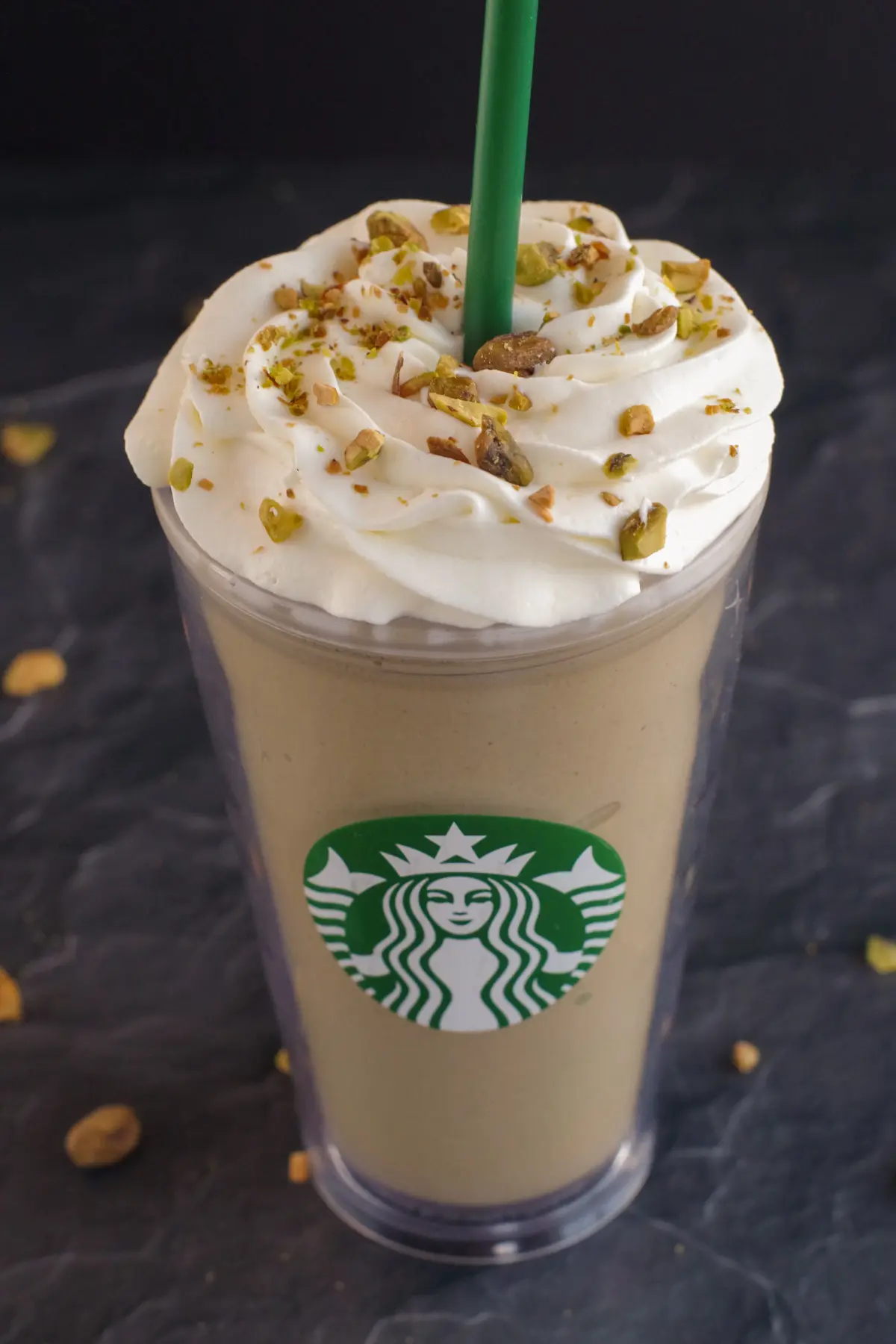 Pistachio Frappuccino in Starbucks cup on black surface with pistachios around